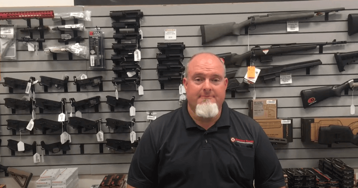 Bob Bailey in gun store discussing AIM Weapons Grade CLP Videos with various firearms on display.